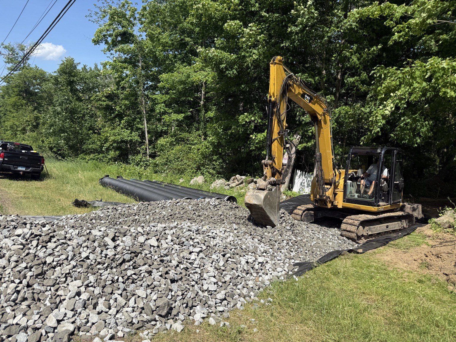 Before image of driveway entrance with excavator and gravel stockpile